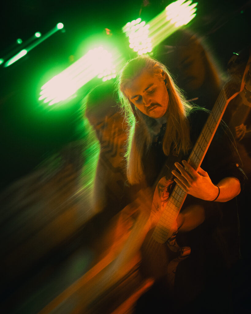 A bassist plays before stage lights with a blur effect.